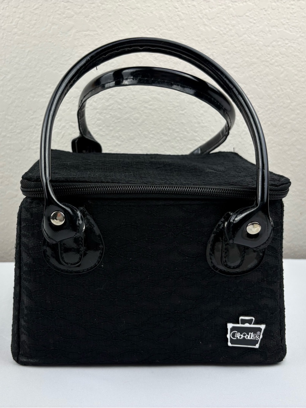 Caboodles patent faux leather makeup case covered with black lace.